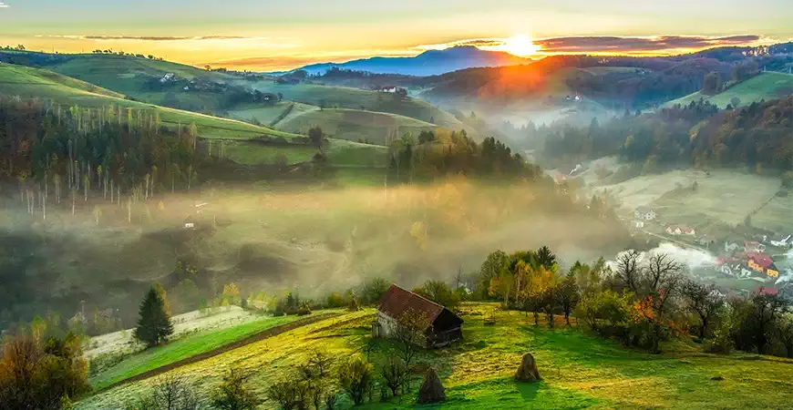 Peisaj din Bucovina cu dealuri verzi, păduri și sat tradițional